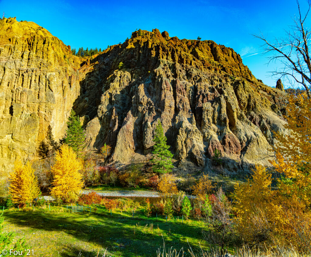 Rugged rock formation above colorful autumn trees and winding trail under clear blue sky wallpaper