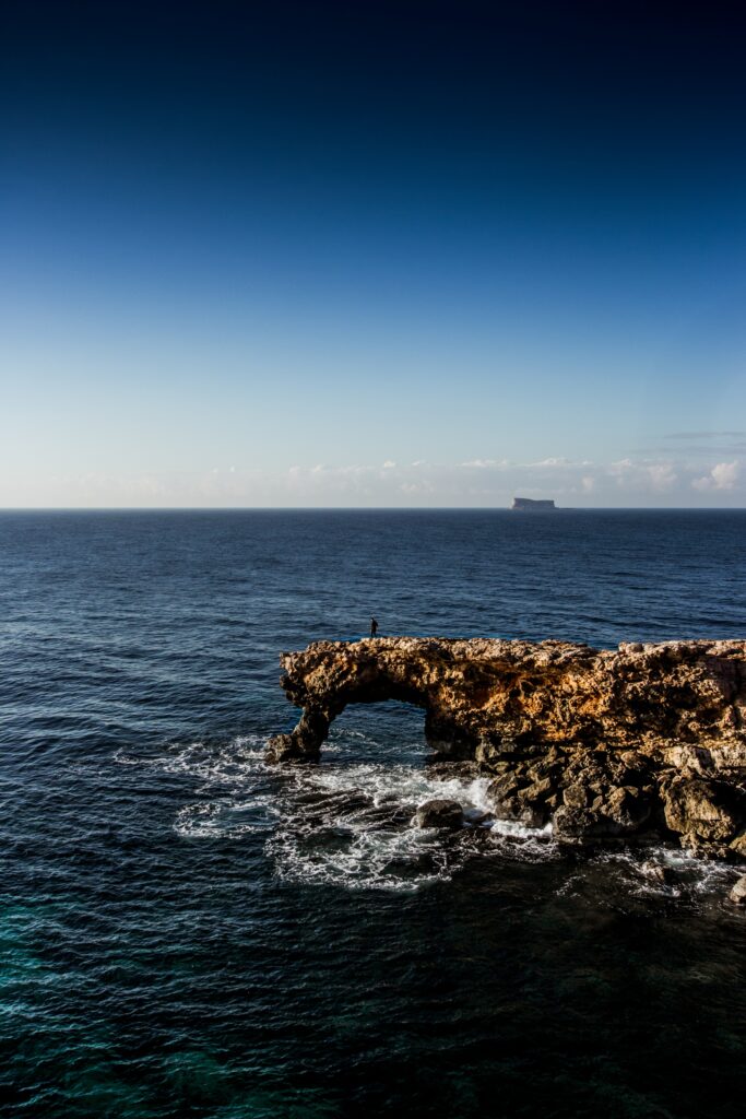 Rugged rock formation by calm sea with gentle waves and deep blue sky wallpaper background