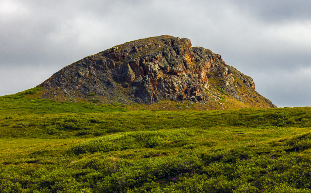 Rugged rock formation on green grassy slope with cloudy sky natural landscape wallpaper background