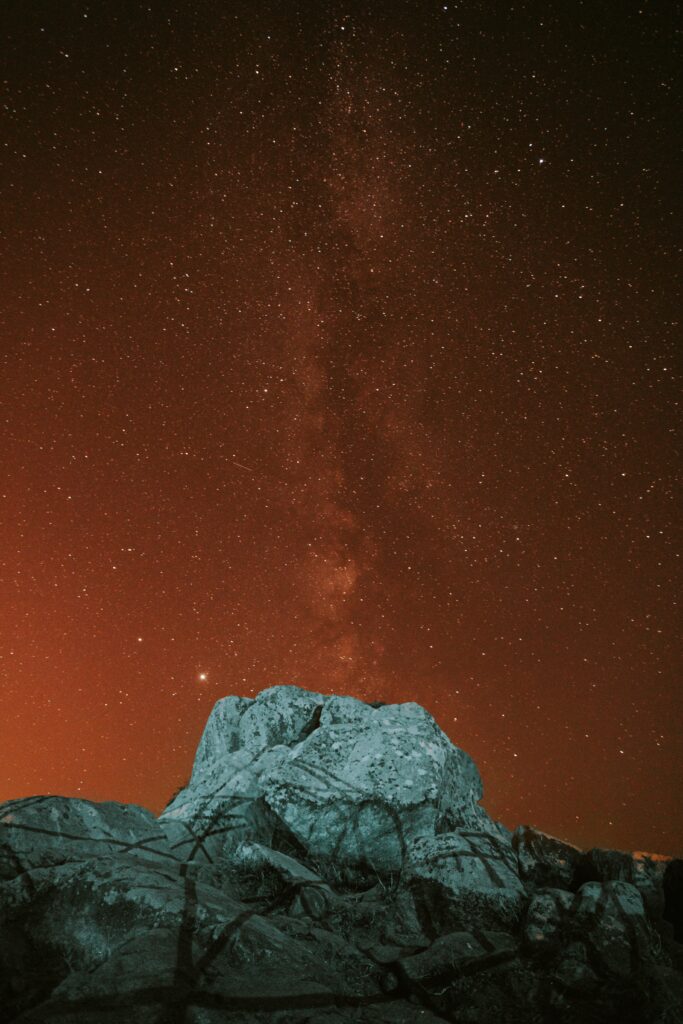 Rugged rocks under glowing nebula and starry night sky with deep space hues wallpaper background