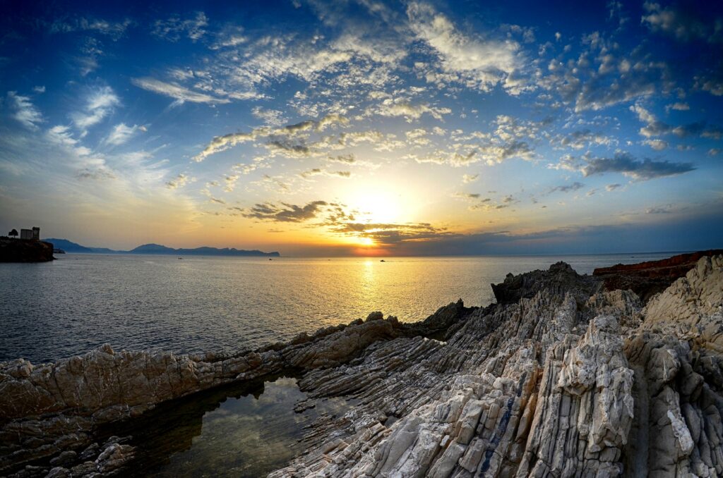 Sunset over rocky coast with dramatic stone formations calm sea and vibrant golden clouds wallpaper