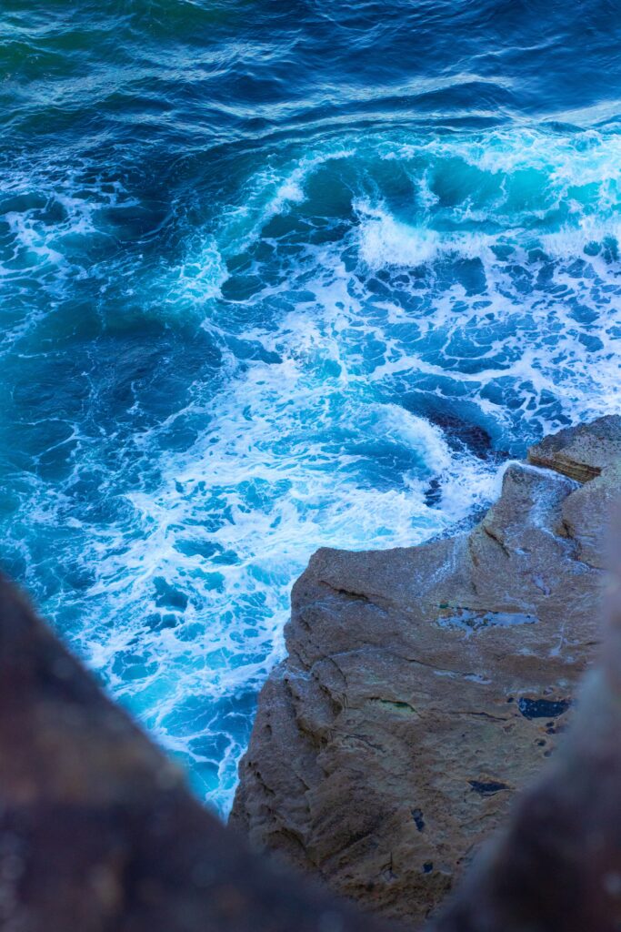 Rugged stone cliffs meet foamy blue waves in a vibrant wild coastal seascape wallpaper background