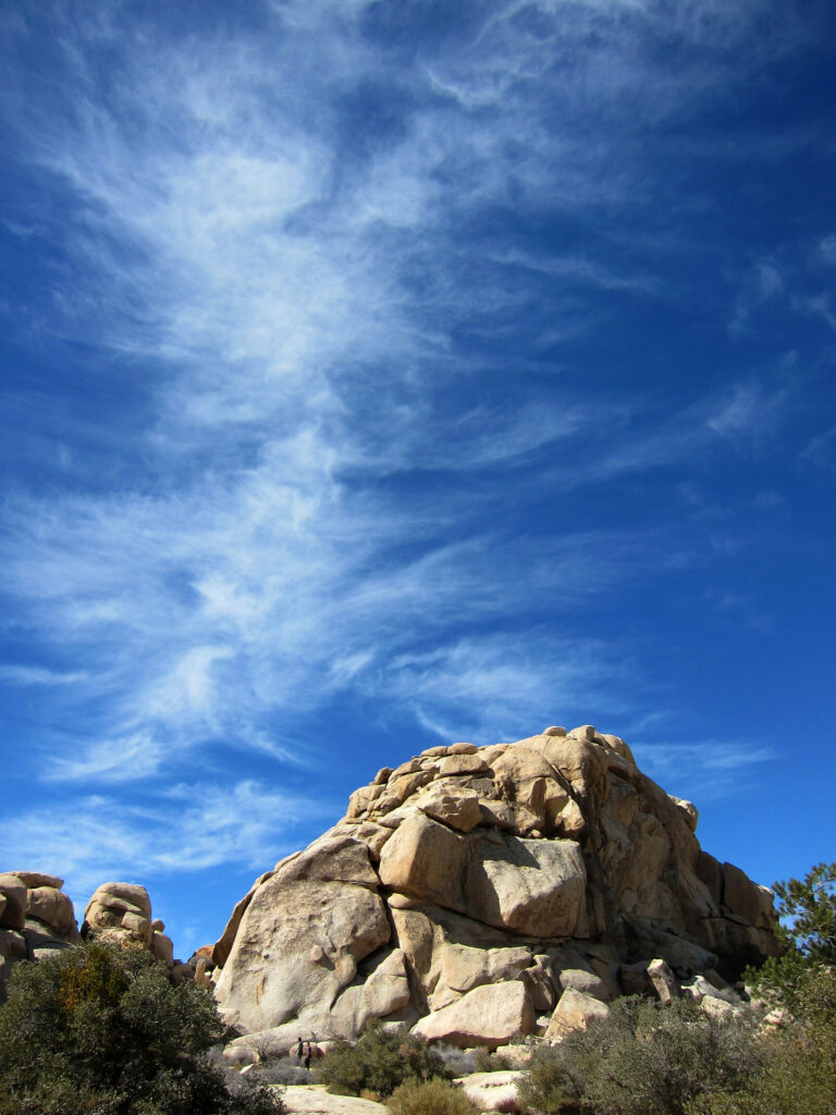 Rugged stone formation under vivid blue sky with wispy clouds and green bushes outdoors wallpaper