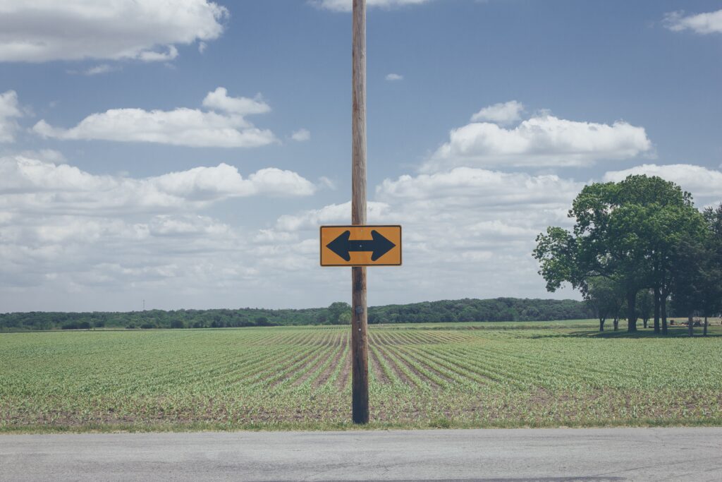 Green field with crops under blue sky and central utility pole showing yellow direction sign Wallpaper