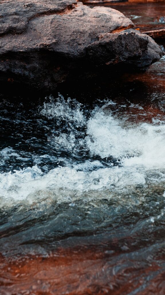 Water rushing over smooth stones and rugged rocks with earthy tones and cool blue hues wallpaper