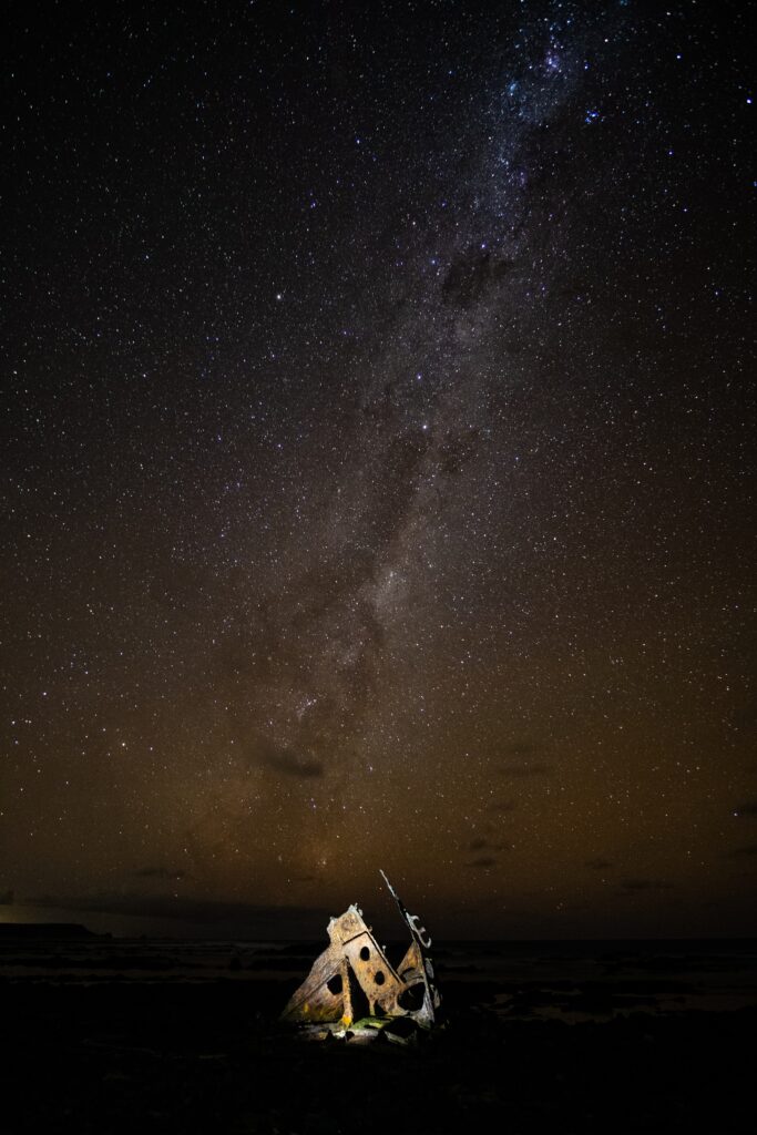 Rusty shipwreck debris under vibrant Milky Way starry night sky dramatic wallpaper background