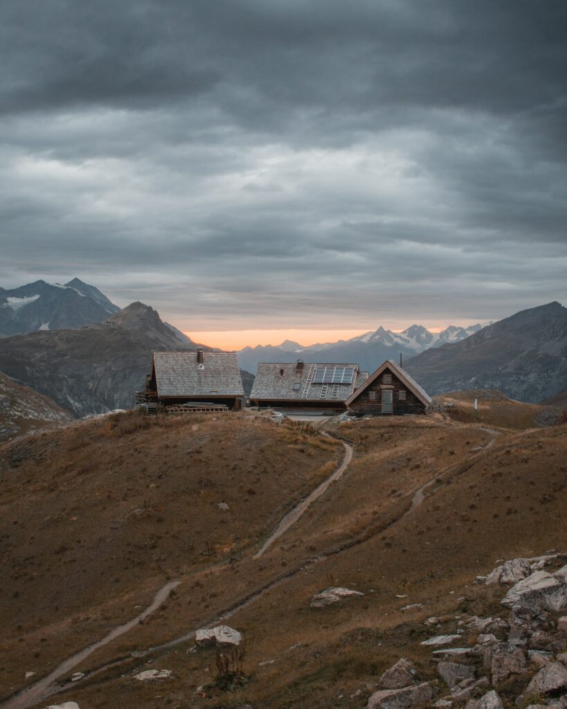 Rustic hillside houses with winding paths and dramatic mountain peaks under cloudy sky wallpaper
