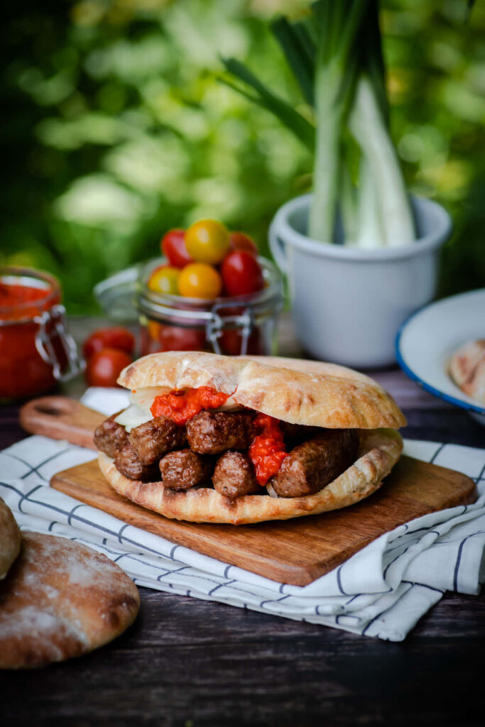 Rustic burger with juicy ćevapi sausages red relish fresh flatbread spring onions cherry tomatoes outdoors Wallpaper
