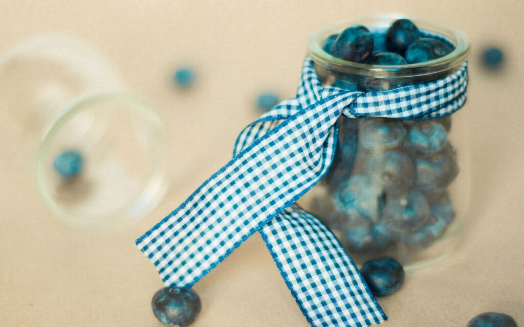 Glass jar of fresh blueberries with blue white checkered ribbon rustic wallpaper background