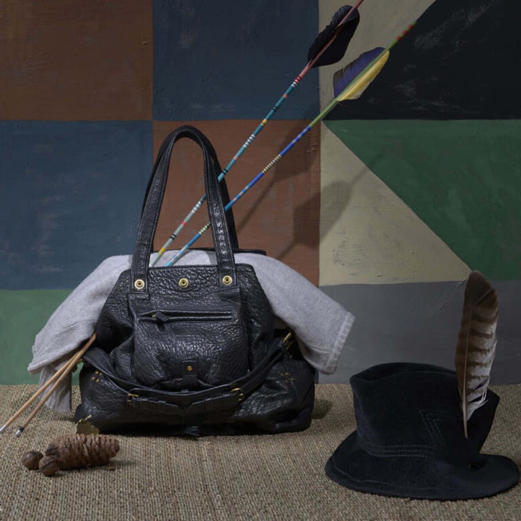 Rustic boho still life with black Jérôme Dreyfuss Billy leather bag arrows feathered hat pinecone Wallpaper