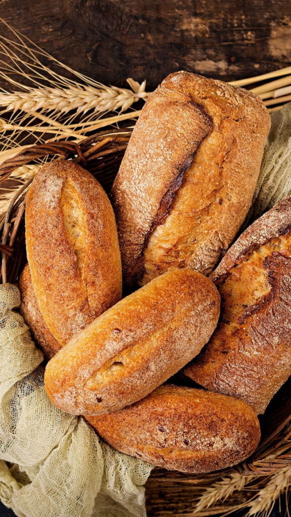 Rustic golden brown breads in woven basket with wheat stalks on wooden linen background Wallpaper