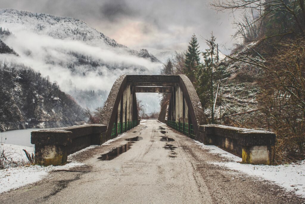 Rustic bridge to snow-covered mountains misty forest wet road bare trees serene winter wallpaper