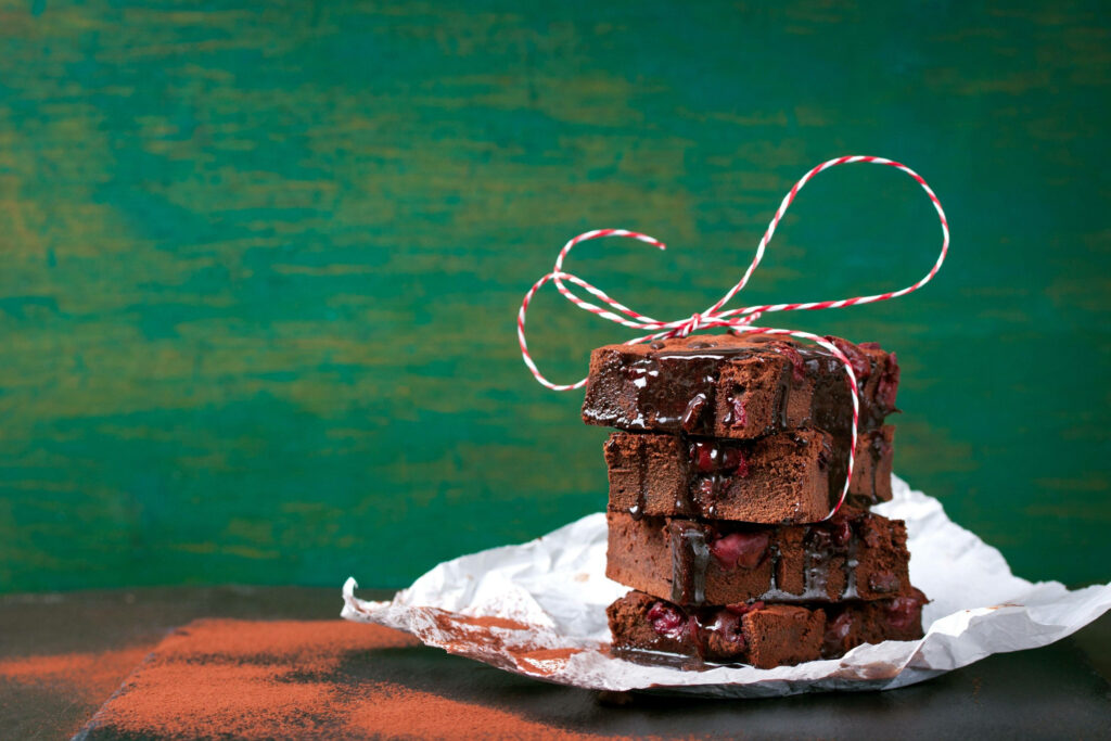 Stack of rich brownies with chocolate powder on parchment paper rustic green brown background Wallpaper