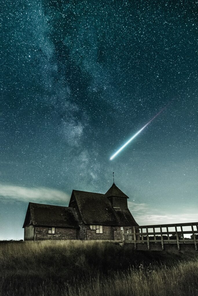 Rustic building under starry night sky with streaking meteorite and wooden bridge at night Wallpaper