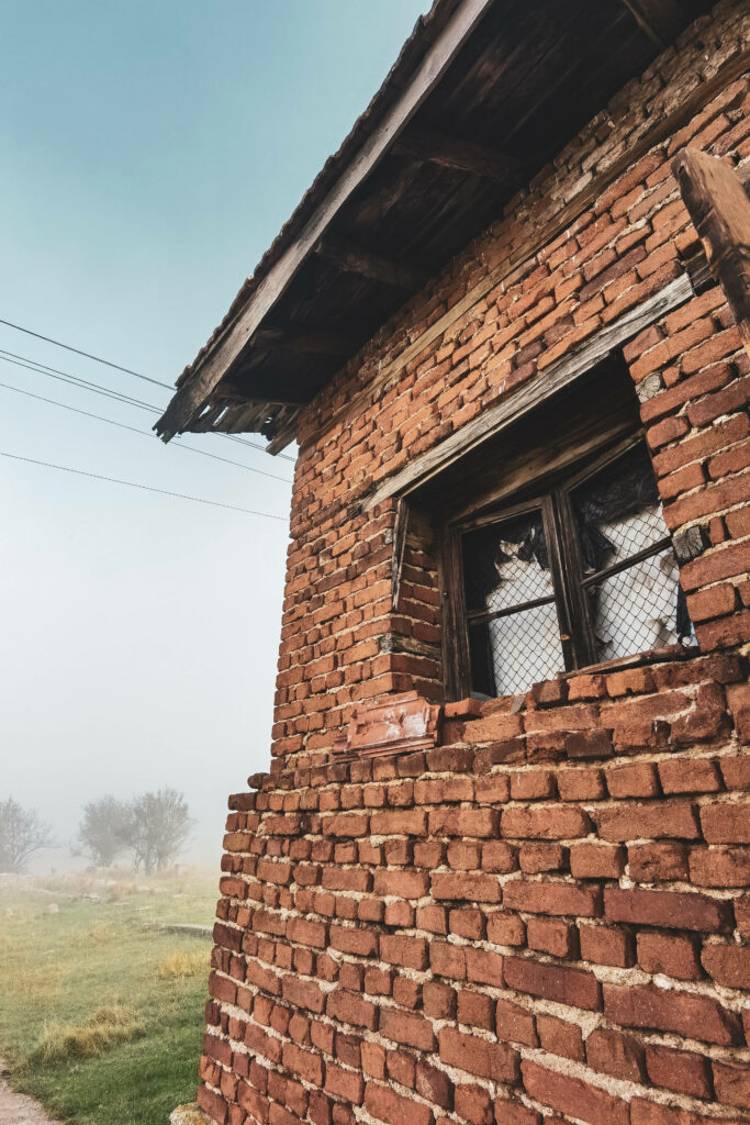 Old Bulgarian brick house with rustic wooden window in misty countryside wallpaper background