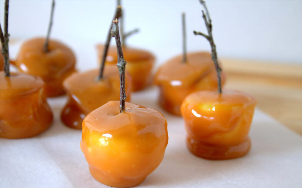 Caramel apples with glossy golden coating on parchment paper rustic autumn treat wallpaper background