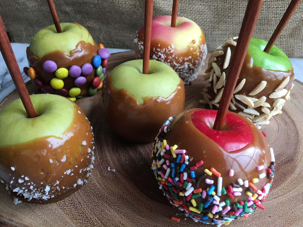 Glossy caramel apples with sprinkles nuts and candies on rustic wooden table festive wallpaper