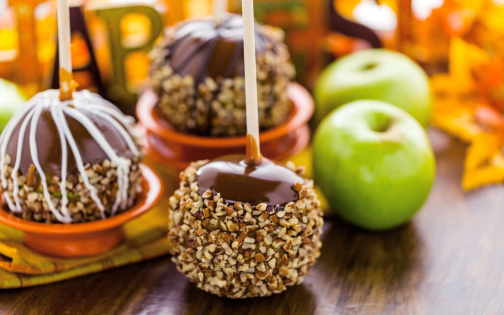 Caramel apples with nuts and chocolate on rustic wood with green apples and autumn leaves background Wallpaper