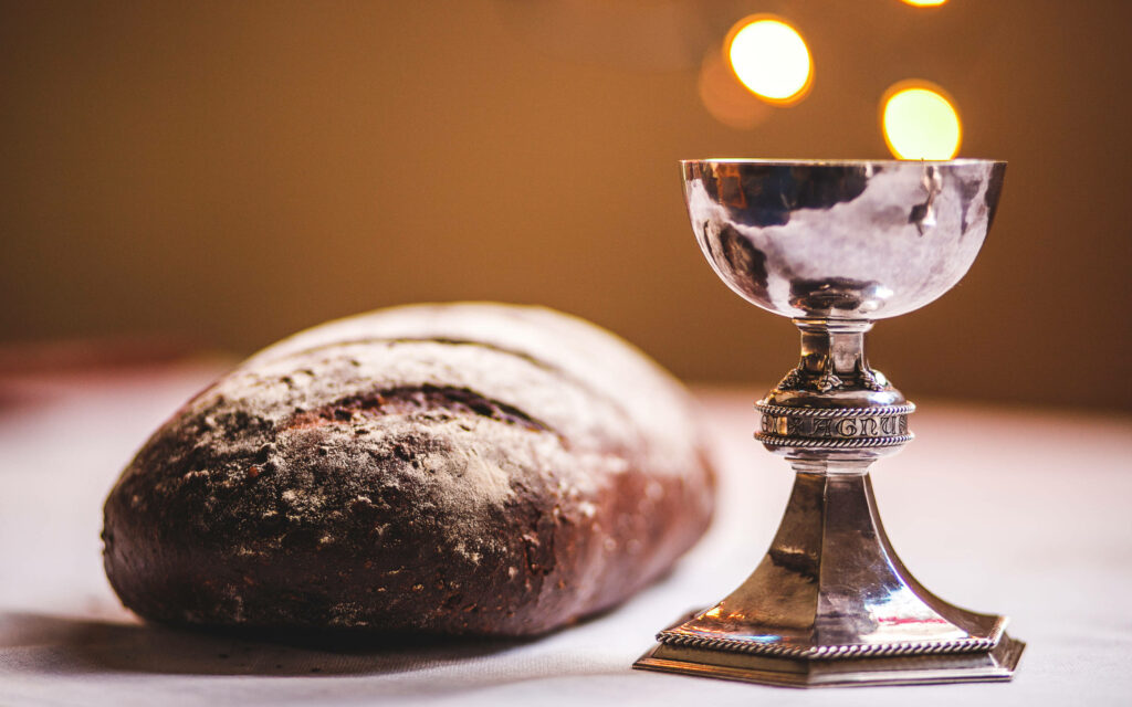 Rustic Catholic bread and silver chalice on white cloth symbolizing Holy Eucharist Communion Wallpaper