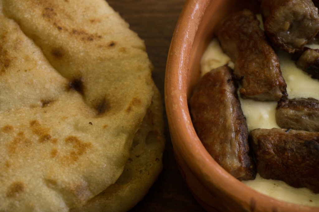 Ćevapi sausages in rustic clay dish with fresh pita bread rich textures golden brown tones wallpaper