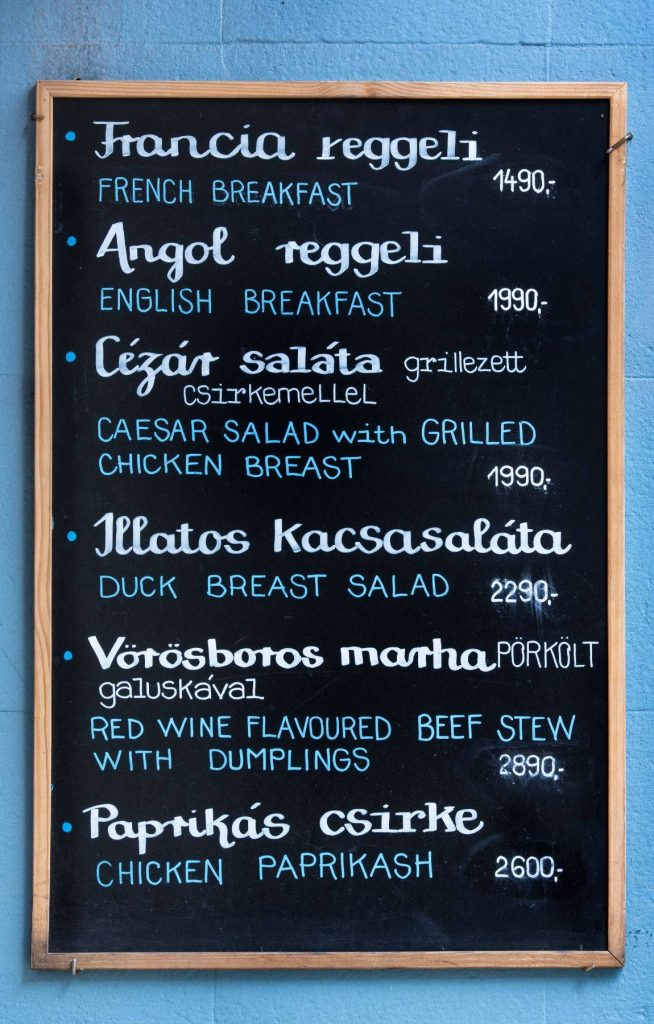 Rustic wooden chalkboard menu with Hungarian English food options on vibrant blue wall wallpaper