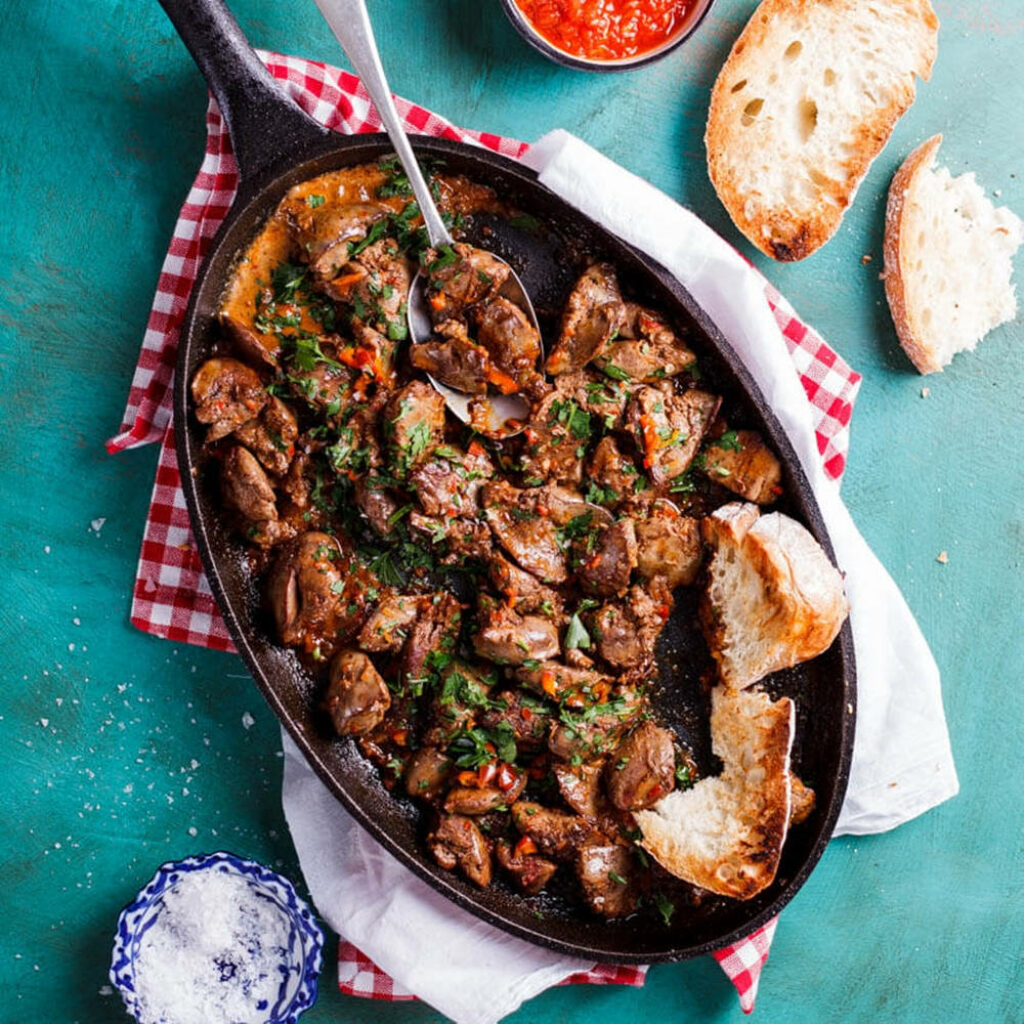 Rustic skillet of herb chicken livers with crusty bread on teal background with red cloth Wallpaper