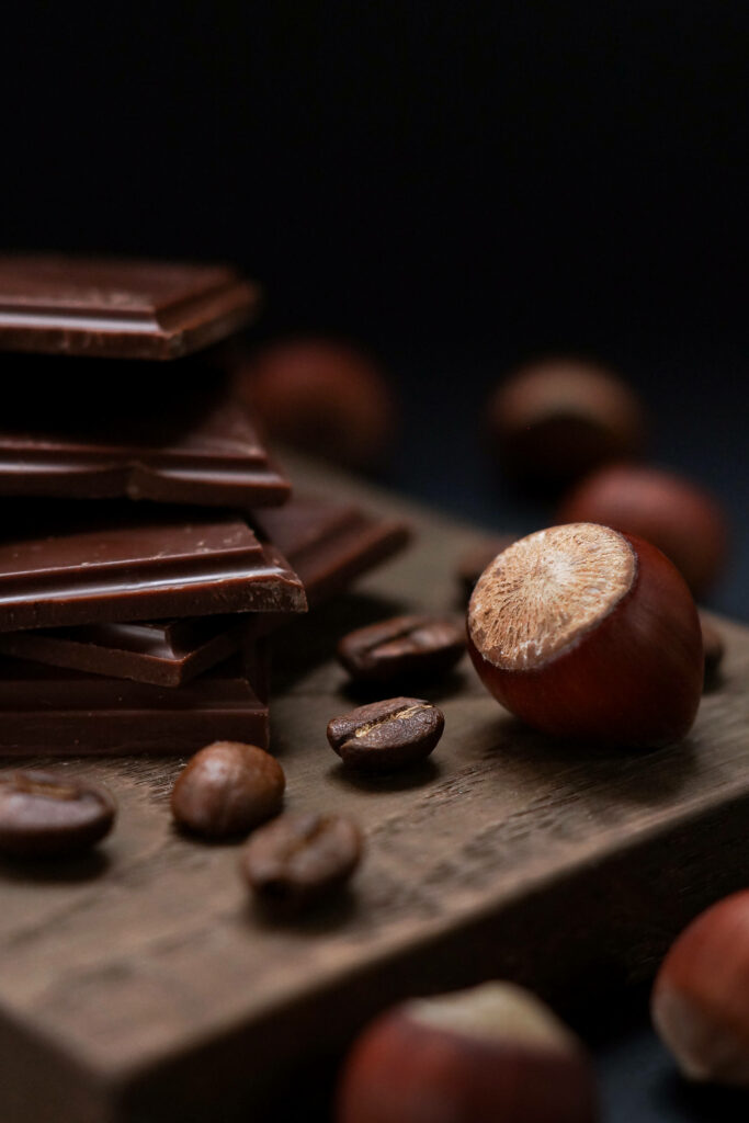 Stacked smooth chocolate bars with hazelnuts and coffee beans on rustic wooden surface background Wallpaper