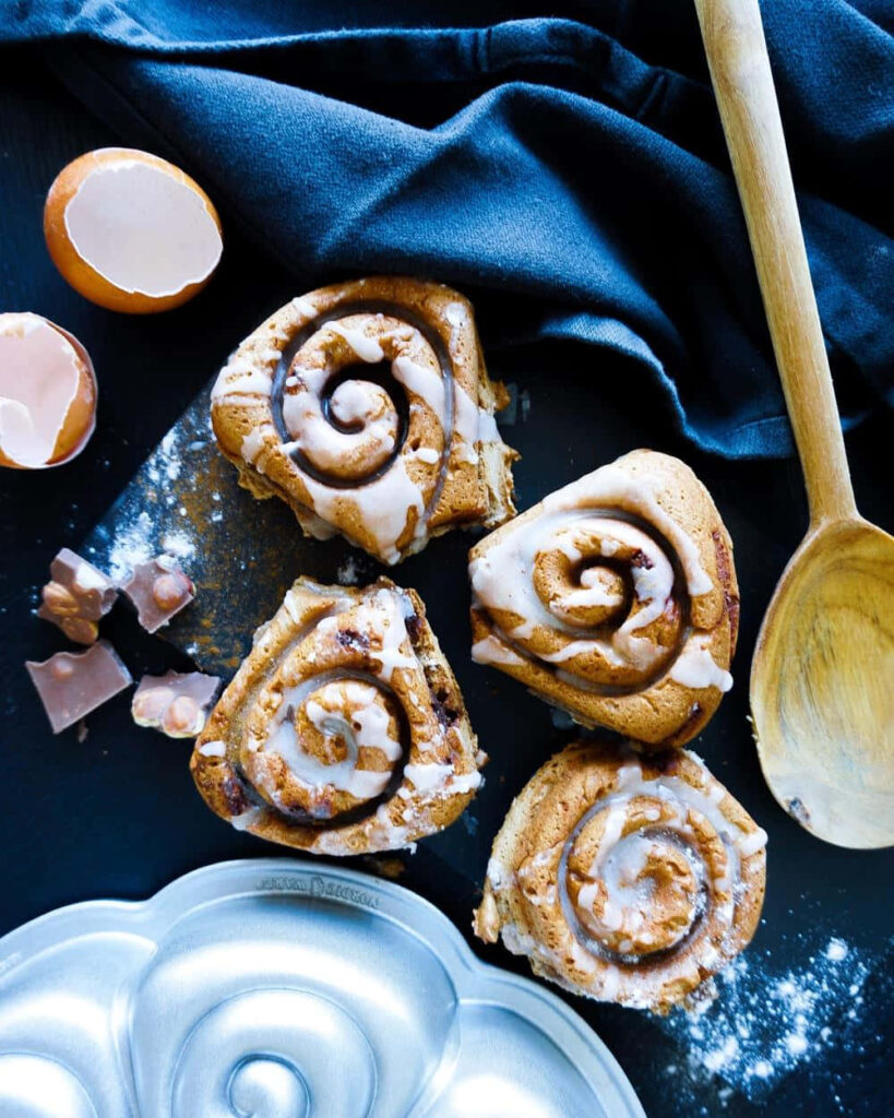 Freshly baked cinnamon rolls with icing on dark surface rustic kitchen scene wallpaper background