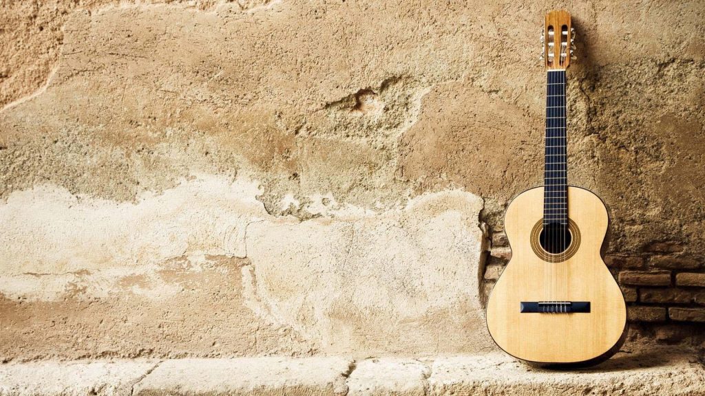 Classical guitar with warm tones leaning on rustic stone wall inspiring music skills wallpaper