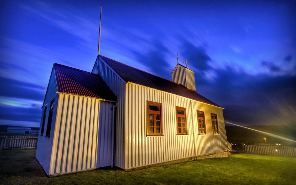 Rustic corrugated metal building bathed in sunlight with dramatic clouds and deep blue sky Wallpaper
