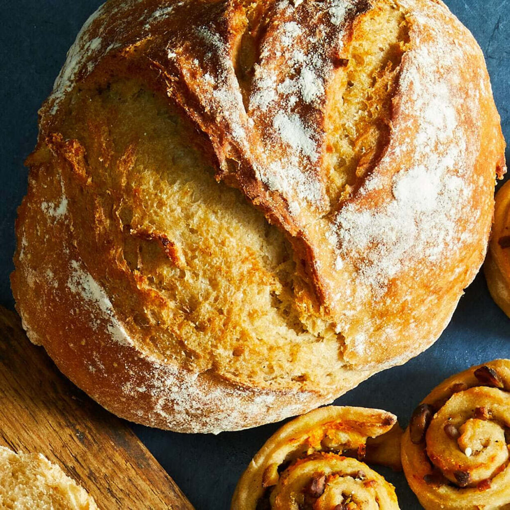 Rustic Crusty Bread Boule Surrounded by Fresh Pastries - Bakery Wallpaper