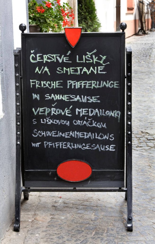 Rustic outdoor chalkboard menu on cobblestone street promoting chanterelle and pork dishes Wallpaper