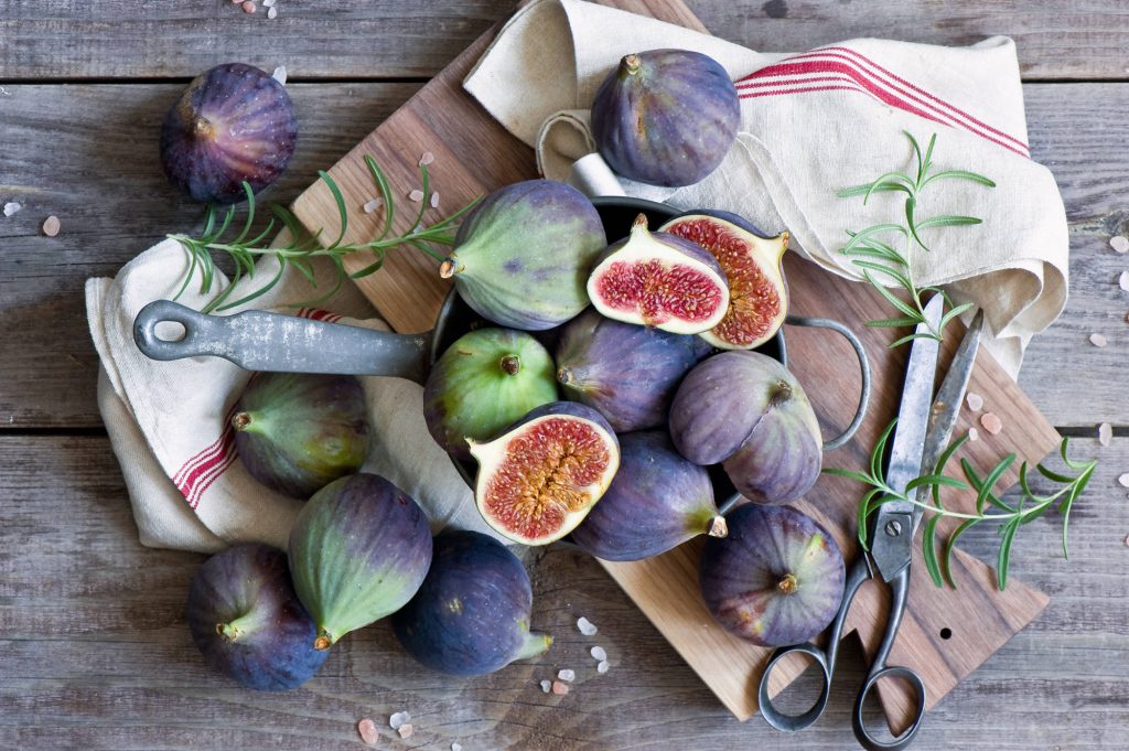 Rustic flat lay with fresh purple green figs halved in vintage pot on weathered wood background Wallpaper