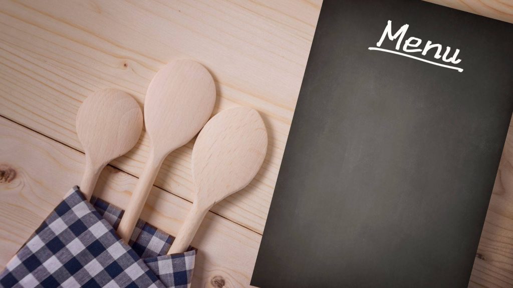 Rustic food wallpaper with wooden spoons in gingham napkin and blank black menu board background