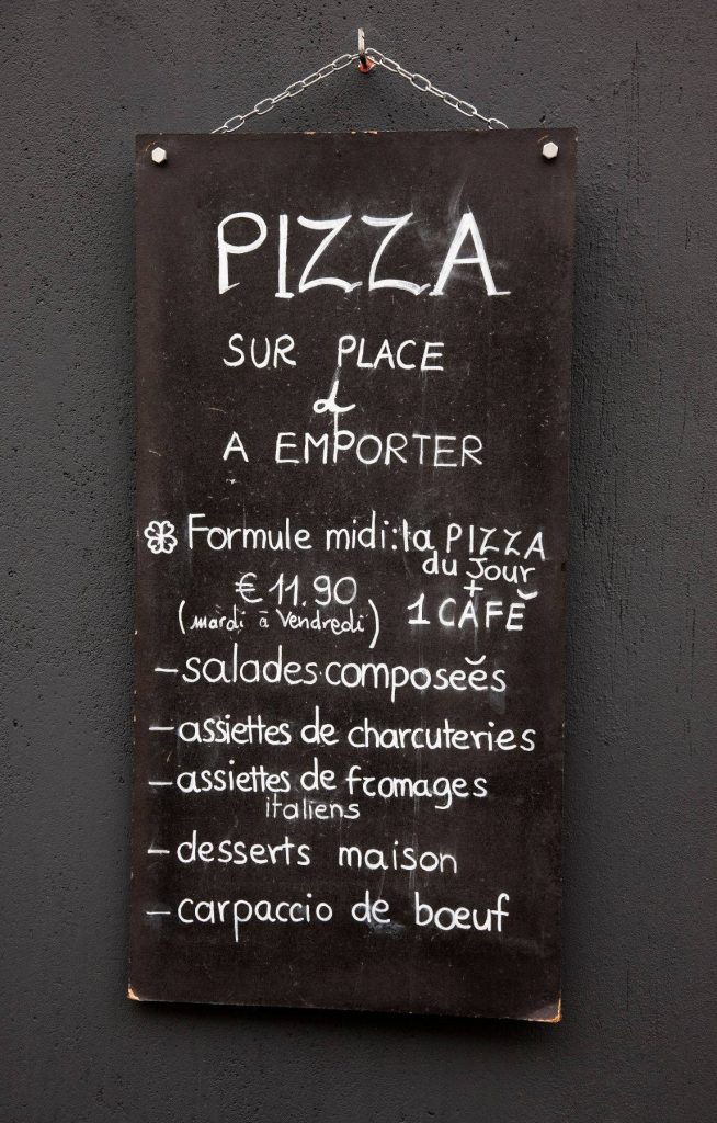 Chalkboard menu with French pizza specials on dark textured wall in rustic modern café interior Wallpaper