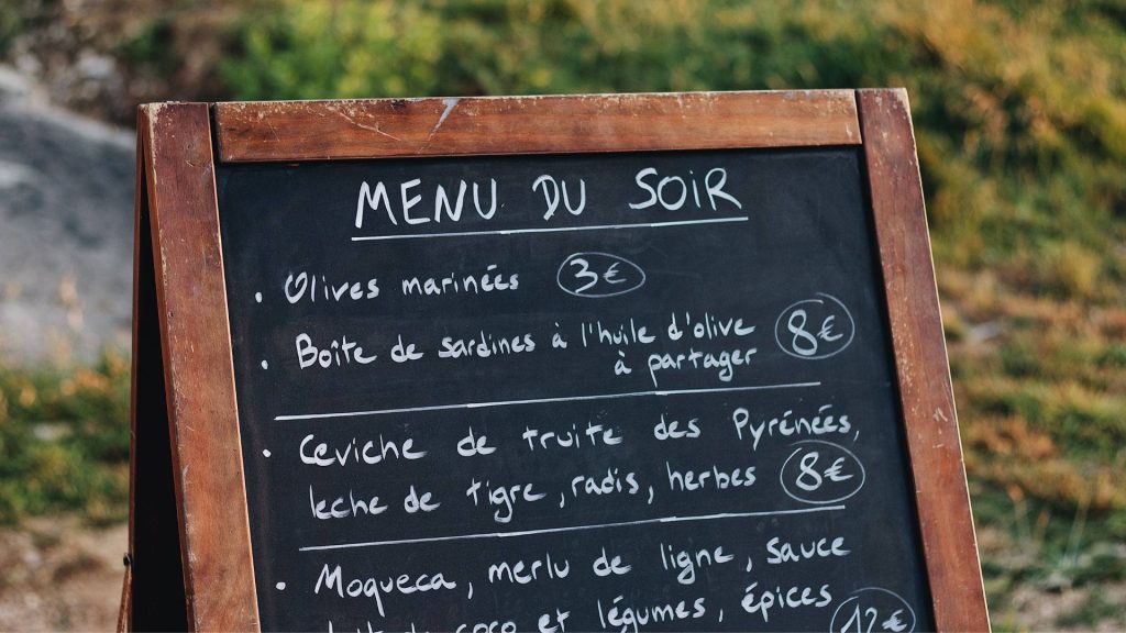 Realistic photo of outdoor French restaurant menu board with handwritten dinner options in wood frame Wallpaper