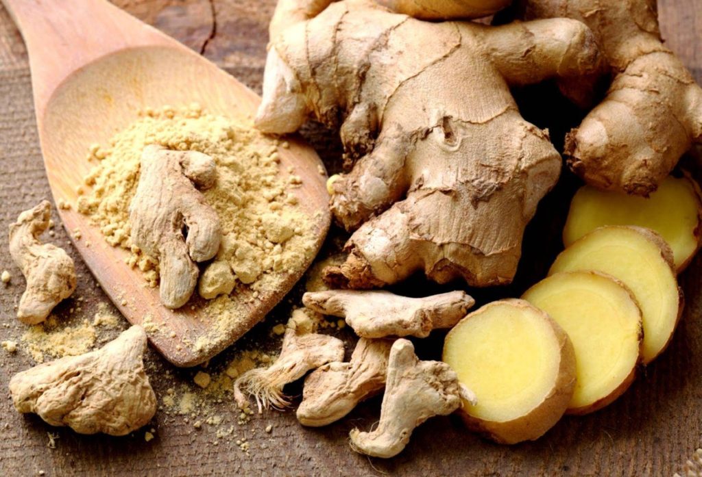 Rustic wallpaper with fresh ginger rhizomes sliced and powdered on wooden textured background