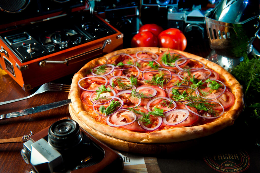 Delicious fresh tomato and red onion pizza on rustic table with vintage cameras food photography Wallpaper