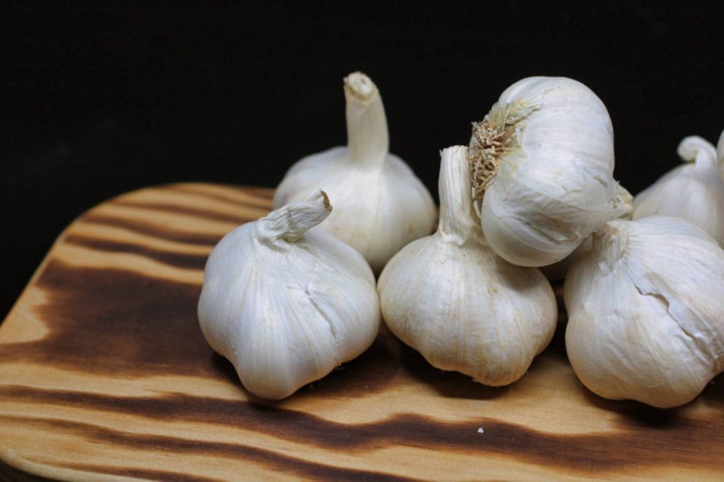 Close-up of fresh whole garlic bulbs on dark wood with black background rustic cooking wallpaper