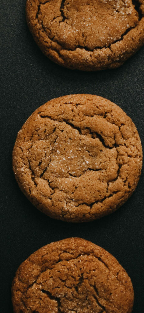 Close-up of golden brown cracked cookies with sugar dusting on dark matte background for food lovers Wallpaper