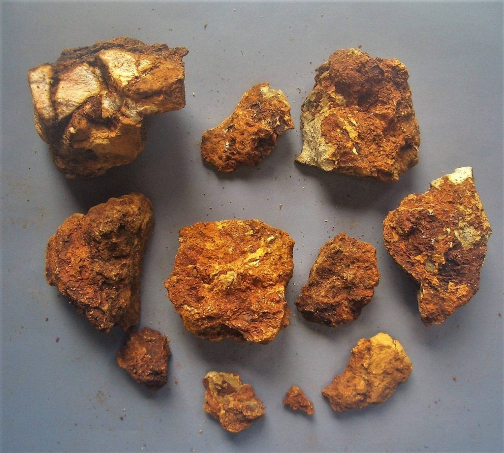 High-angle photo of raw goldmine lode pieces with rusty orange textures on gray background Wallpaper