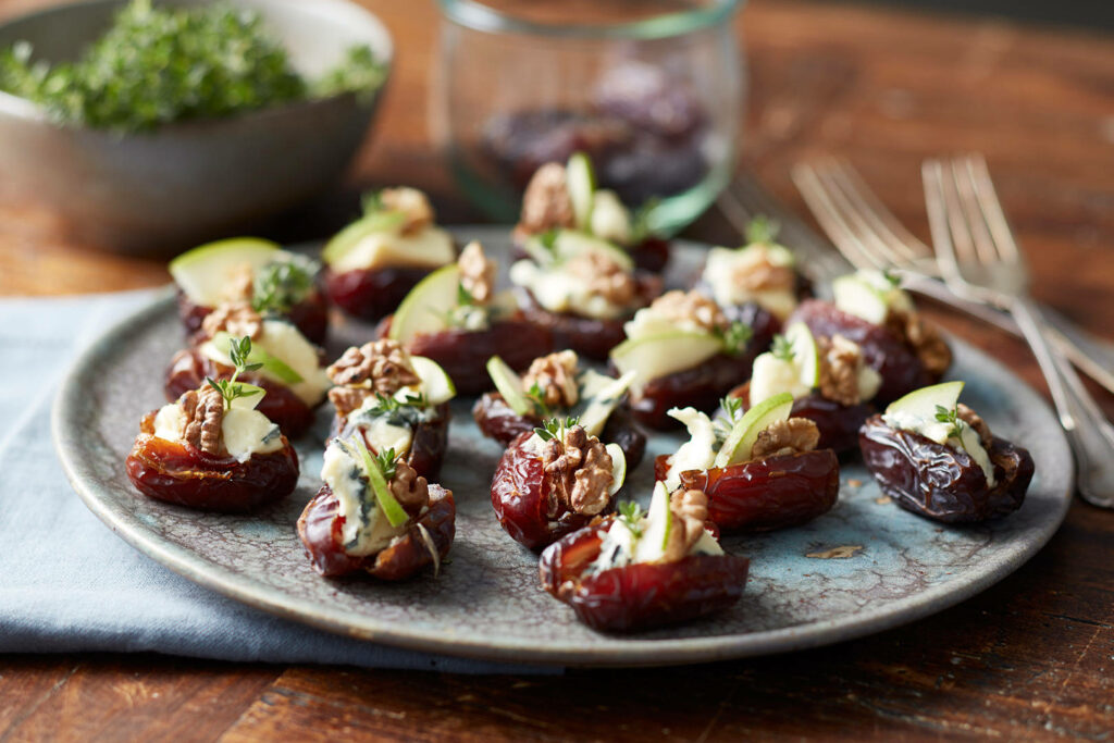Rustic table setting with cheese stuffed dates walnuts apple slices and fresh herbs gourmet cuisine Wallpaper