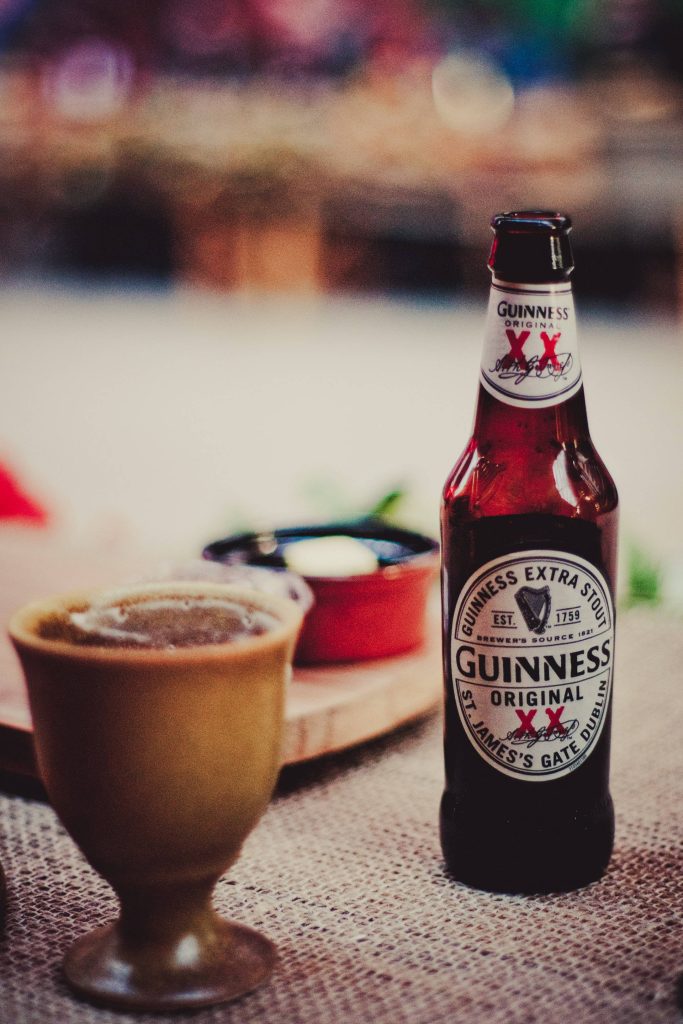 Rustic wallpaper with Guinness Original Extra Stout bottle and dark goblet in warm moody light