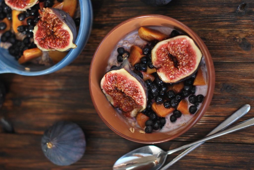Two rustic bowls of creamy porridge topped with fresh figs blueberries and golden peaches on wood Wallpaper