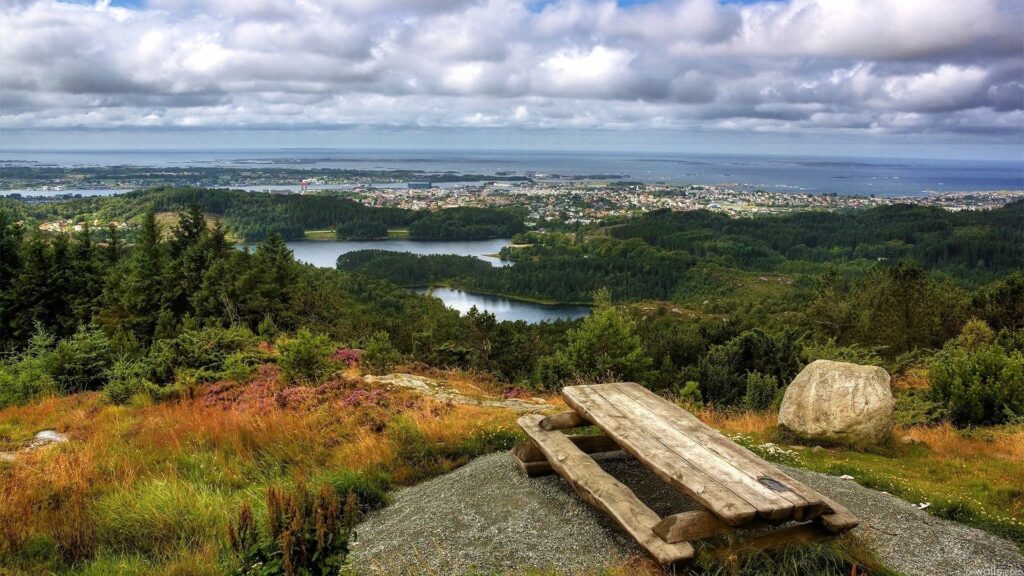 Rustic wooden table and benches on hilltop with islands city lakes forests and dramatic clouds Wallpaper
