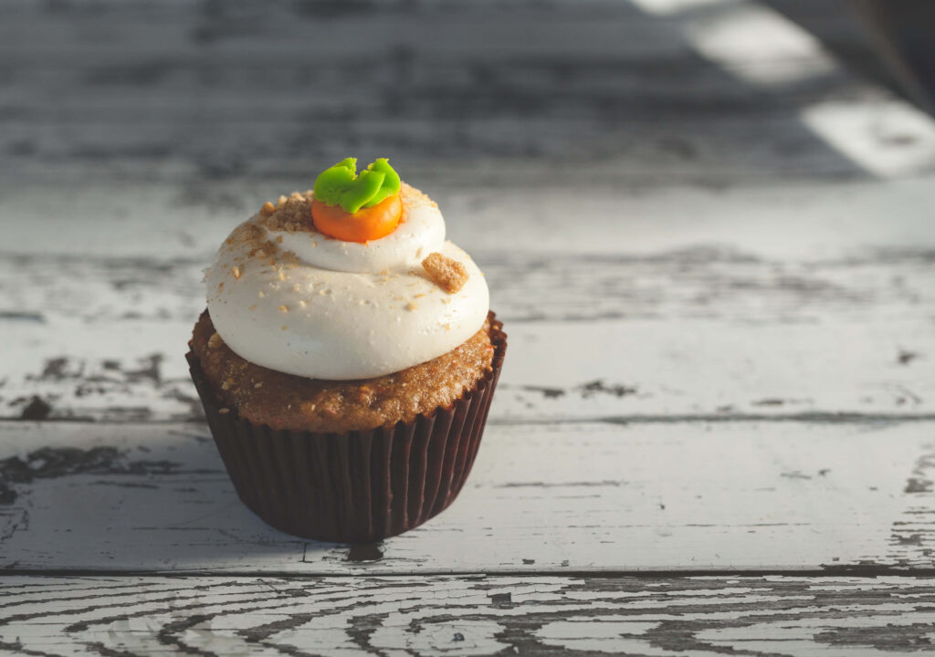 Homemade cupcake with white frosting and carrot decoration on rustic wooden background Wallpaper