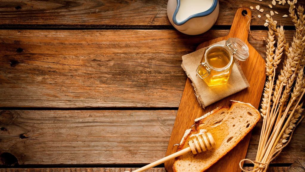 Rustic honey jar with wooden dipper and bread on board with wheat stalks and pitcher background Wallpaper