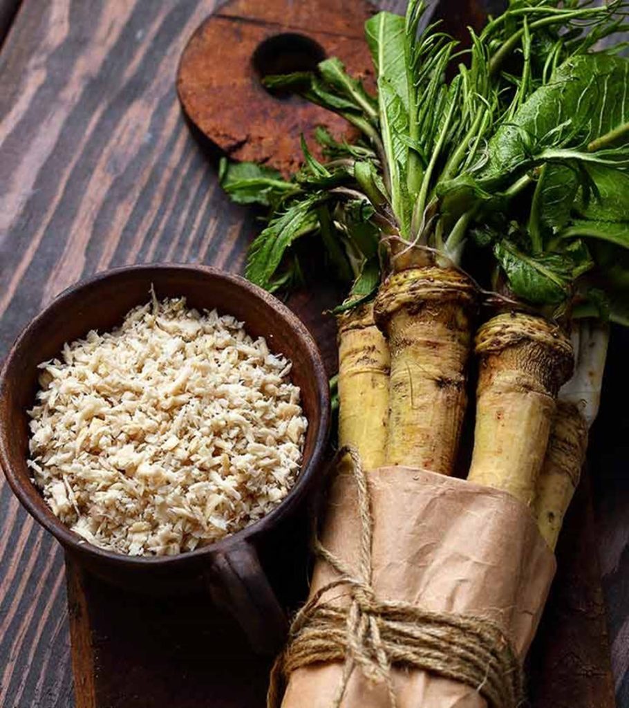 Rustic wallpaper with dark wooden bowl of grated horseradish and fresh horseradish roots