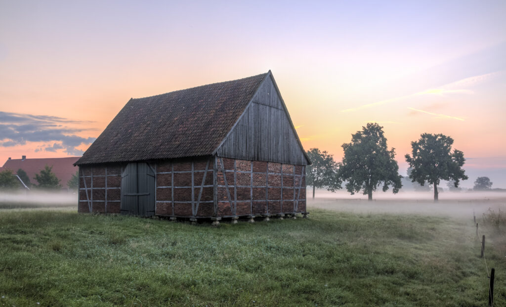 Rustic house in foggy grassy field at sunrise with pastel sky and peaceful rural landscape wallpaper