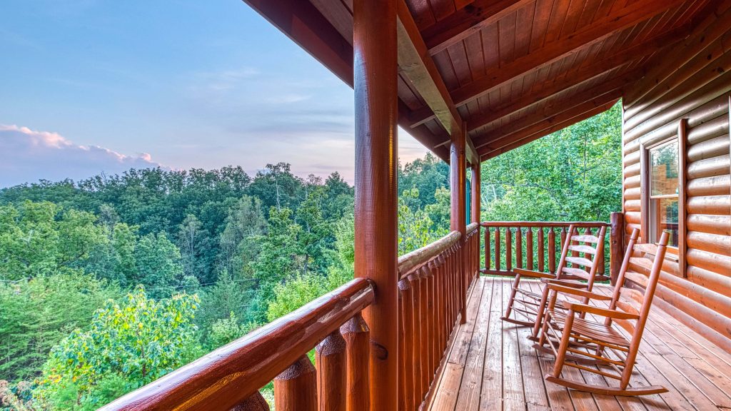 Rustic log cabin porch with wooden rocking chairs overlooking lush green forest canopy serene view Wallpaper